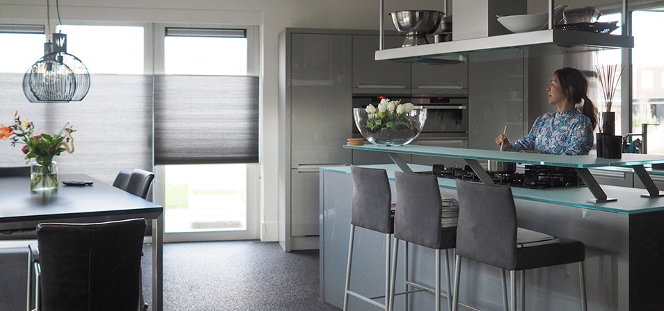 duo plisségordijnen moderne keuken glazen keukenblad bar grijze barstoelen modern interieur woonkeuken